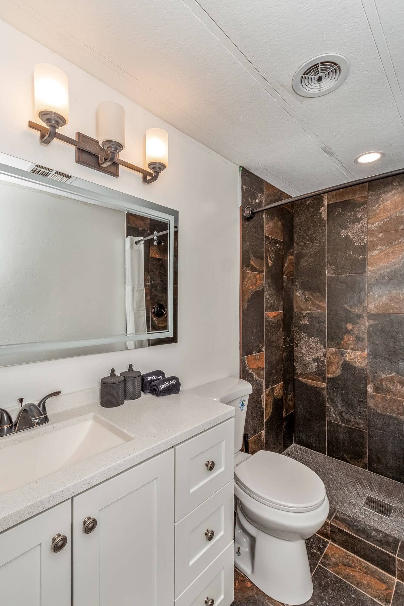 A bathroom with a stone-tiled shower, polished vanity and rolled towels